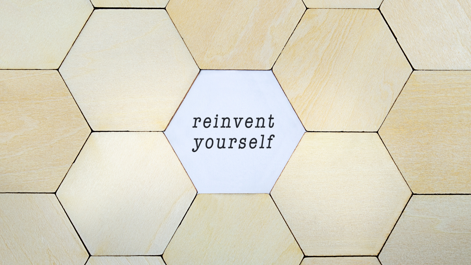 Wooden hexagon missing from puzzle, revealing the word reinvent yourself in a conceptual image of personal growth and self discovery